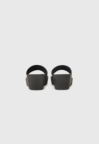 Sandale negre cu toc gros în formă de wedge și curea rotundă la spate, având un finisaj mat și o formă geometrică. Design simplu și minimalist.