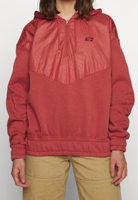 Červená mikina s kapucí s texturovanou, lesklou horní částí, polo-zip vpředu a žebrovanými manžetami a pasem pro pohodlné nošení.