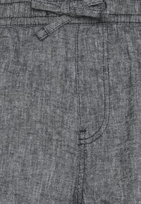 Zbliżenie na szare materiałowe spodnie z elastycznym paskiem i widocznymi szwami kieszeni z czarnymi detalami sztukowania.