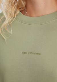 Olivově zelená mikina s žebrovaným kulatým výstřihem a jemnou strukturou. Na přední straně se nachází vytlačené logo "Marc O'Polo DENIM".