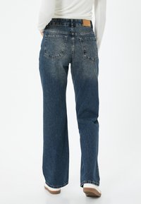 Kapeat farkut keski sinisessä, joissa on viisi taskua, hienovarainen kulutus ja nahkapaikka takavyötäröllä.