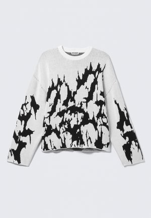 Hvid strikket sweater med et sort abstrakt mønster på forsiden og ærmerne. Designet er løstsiddende med rund halsudskæring.