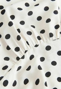 Tissu blanc à pois noirs avec un détail de couture froncée créant une texture à volants.