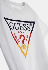Vit bomull T-shirt med en triangulär broderad logotyp i marinblått, rött och gult, med texten "GUESS," "WASHED," och "JEANS."