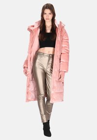 Długa różowa kurtka puchowa o prążkowanej fakturze, wyposażona w kaptur i zatrzaski. Dopasowana do niej błyszczące, metaliczne srebrne spodnie.