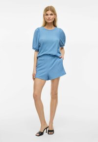 Top blu con fantasia, maniche corte a puff e pantaloni corti abbinati, realizzato in un tessuto leggero. Tacchi neri open-toe completano l'outfit.