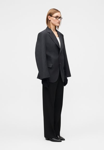 Grå nålestribet oversize blazer, sorte bukser med vide ben, sorte handsker og minimalistiske sorte sko; glat tekstur og struktureret design.
