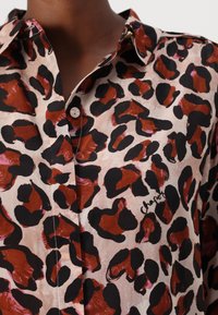 Leopard print button-up shirt featuring a blend of earthy brown and black patterns on a light beige background with a smooth texture.