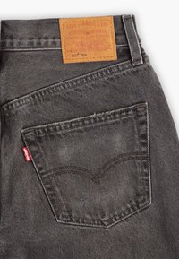 Jeans en denim gris foncé avec une étiquette en cuir marron clair affichant "Levi Strauss & Co." et un onglet rouge sur la poche arrière, mettant en valeur les détails de la couture.