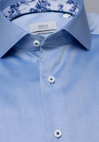 Camicia a righe di colore azzurro chiaro, realizzata in tessuto liscio. Presenta un colletto interno a motivo in contrasto e bottoni bianchi con accenti blu.