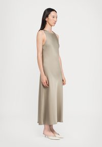 Satin-muotoinen, olkaimeton mekko vaaleassa beigeissä väreissä, nilkkapituinen, jossa on tiukka korsetiosuus ja liehuva hame. Yhdistetty kärjellisiin, neutraalin värisiin korkokenkiin.