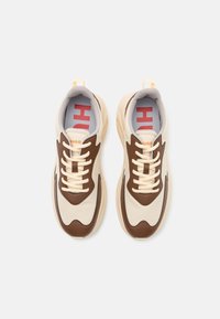 Smukłe sneakersy wykonane z kremowych i brązowych materiałów, z teksturowanymi akcentami, grubymi sznurowadłami oraz logo umieszczonym na języku; okrągły design podeszwy.
