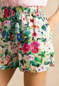Gėlių rašto šortai iš lengvos medžiagos, su spalvingu rausvų, mėlynų ir žalių gėlių piešiniu; elastinga juosmens juosta; šoniniai kišenės; laisvas siluetas.