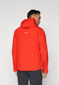 Veste imperméable rouge avec capuche, présentant une texture lisse et un logo au dos. Le design inclut des poignets réglables et une coupe élégante.
