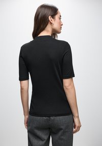 Sort kortærmet polo skjorte lavet af bomuld, med en klassisk krave og en tætsiddende design; parret med strukturerede grå bukser.