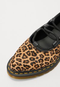 La scarpa con stampa leopardata presenta una parte superiore in pelo di mucca texturizzato, lacci neri, dettagli neri e una suola spessa in gomma con cuciture arancioni.