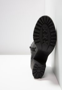 Bottine noire en cuir texturé, semelle plate en caoutchouc avec motif de bande de roulement, et fermeture éclair latérale.