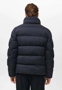 Chaqueta acolchada de color azul marino con cuello alto, que presenta secciones gruesas acolchadas y una textura suave y mate. La vista trasera no muestra logos visibles.