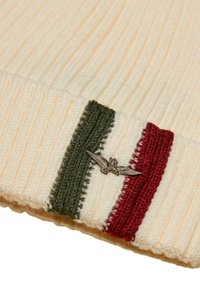 Berretto a coste di maglia color crema con strisce verdi e rosse; presenta un accento di emblema d'aquila argentato sulla parte anteriore. Texture morbida.