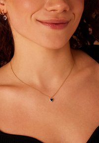 Collar de cadena de oro con un colgante de gema azul en forma de corazón rodeado de pequeñas piedras claras. Textura suave, diseño delicado.