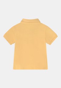 Ljusorange kortärmad polo t-shirt med vikbar krage, sedd bakifrån mot en vit bakgrund.