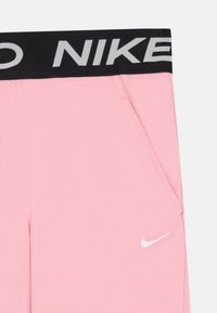 Rozā bikses ar melnu elastīgu jostu, uz kuras ir balta uzraksts "NIKE". Iekļautas sānu kabatas un neliels balts Nike logo uz kājas.