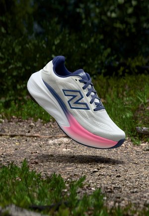 Chaussure de sport blanche et bleue avec un détail de semelle rose flottant au-dessus d'un chemin de gravier entouré de feuillage vert.