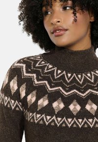 Maglione a maglia marrone con colletto alto, caratterizzato da motivi geometrici in crema e dettagli metallici. Tessuto texturizzato e accogliente con un design aderente.