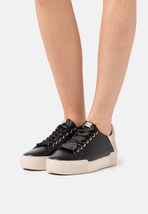 Baskets en cuir noir avec un talon crème, dotées d'œillets dorés et de lacets en satin noir. Semelle en caoutchouc texturée avec un design strié.