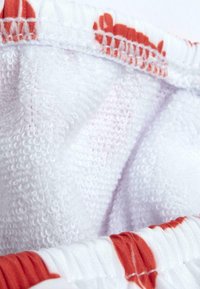 Tessuto di cotone bianco con motivo floreale rosso, dotato di bordo in spugna testurizzata e vita elastica.