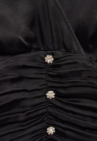 Tissu noir froncé avec couture verticale et trois petits boutons ronds en strass disposés en colonne.