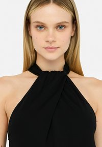 Zwarte halternek top gemaakt van lichte stof, met een geknoopt ontwerp bij de halslijn en een losse silhouette.