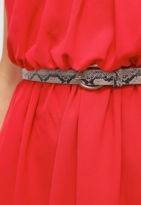 Robe en tissu rouge cintrée à la taille avec une ceinture en cuir texturée imitant un serpent, ornée d'une boucle ronde métallique.