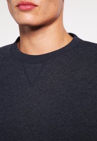 Mörknavy sweatshirt med rund halsringning, som visar en jämn textur och sömdetalj vid axeln. Tyget är mjukt och avslappnat.