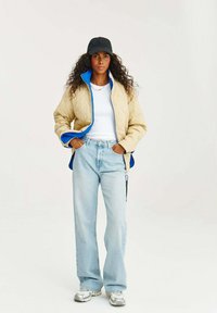 Námořnická prošívaná bunda s modrými akcenty, bílý tričko, světle modré džíny a stříbrné tenisky. Černá čepice a jemný detail náhrdelníku.