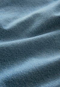 Tejido de mezclilla azul con una textura suave y un sutil patrón tejido, que muestra suaves pliegues y arrugas.
