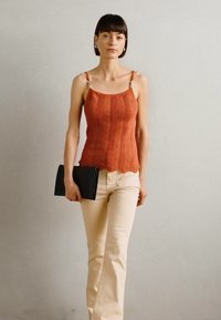 Débardeur couleur rouille avec une texture de vagues diagonales, fines bretelles avec des accessoires en argent. Associé à un pantalon évasé beige clair et une pochette noire.