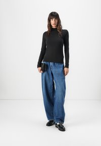 Maglia nera a maniche lunghe abbinata a jeans blu in denim larghi e mocassini neri. La maglia presenta un collo alto, una texture liscia e una silhouette aderente.