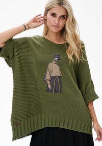 Zielony, oversize'owy sweter z dzianiny z żeberkowymi akcentami oraz grafiką postaci w paski. Posiada okrągły dekolt i luźne rękawy.