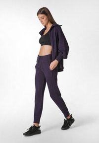 Paarse sportieve sweatshirt met kraag, gecombineerd met bijpassende paarse joggerpants. Zwarte sportbeha eronder. Getextureerde stof, sportief design.