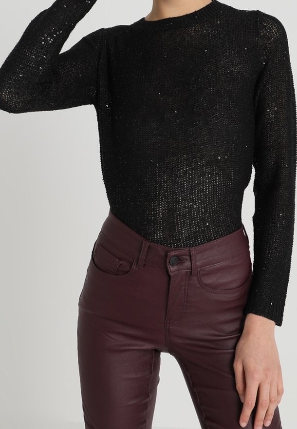 Pull en maille noir à manches longues avec de subtils sequins, associé à un pantalon en cuir bordeaux foncé taille haute porté par une personne.