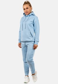 Lichtblauwe hoodie met een kangoeroezak, gecombineerd met bijpassende joggingbroeken. Beide hebben ribbelmanchetten, trekkoorddetails en een zachte textuur.