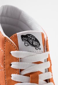 Baskets en suède orange avec lacets blancs et col rembourré. Présentent le logo Vans Off The Wall sur une étiquette blanche près de la languette.