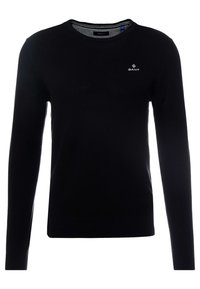 Zwart gebreide trui met een ronde hals, lange mouwen en geribbelde boorden. Heeft een klein wit logo op de borst en een patroonstructuur.