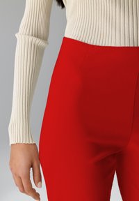 Crème ribbel langemouwen top gecombineerd met hoge rode broeken, zachte textuur, op maat gemaakte pasvorm en verborgen zijzakken.