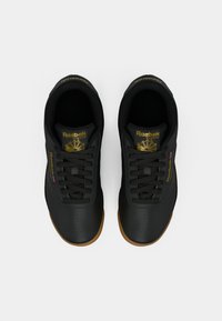 Ténis Reebok pretos com um upper liso, sola de borracha caramelizada e detalhes em dourado no logotipo e na língua. Inclui atacadores pretos e detalhes perfurados.