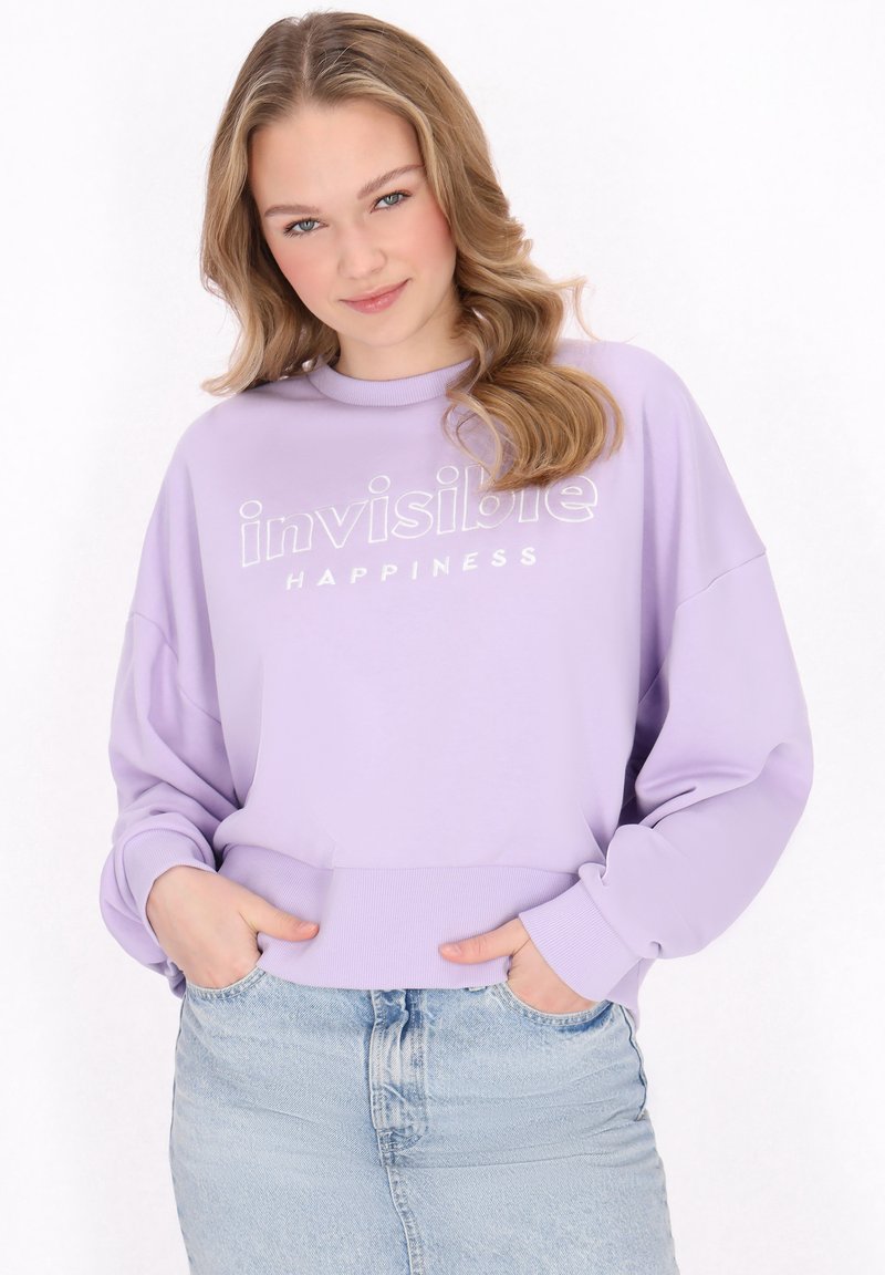 Felpa viola chiaro con la scritta "HAPPINESS invisibile". Presenta un collo rotondo e una vestibilità rilassata, abbinata a una gonna di jeans azzurri chiari.