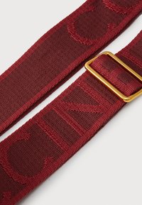 Burgundy fabric belt with a textured finish and embossed lettering, featuring a gold-tone metal buckle.