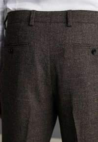 Grau strukturierte Hose mit feinem Muster, ausgestattet mit zwei Gesäßtaschen und schwarzen Knopfakzenten. Modische Passform mit einem Standardbund.