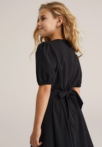Crna haljina sa kratkim puff rukavima, uskim korzetom i detaljem s vezanjem u struku, izrađena od glatkog materijala s lepršavom suknjom.